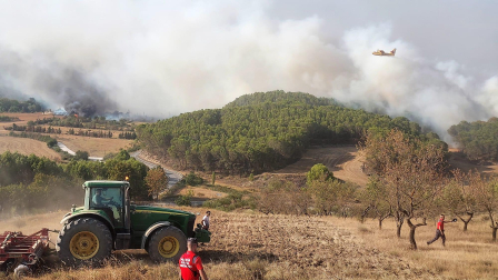 Desde lo alto del pueblo varias personas observan con preocupación las llamas acercarse y a los medios aéreos intentando sofocar el fuego