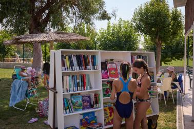 Dos niñas buscan un libro y releen en la biblioteca móvil instalada en la piscina