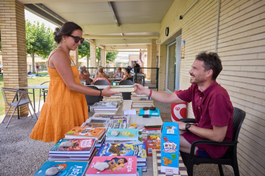 El bibliotecario de Mendigorría, Xabier Elduayen, atiende a una vecina de Mendigorría en la biblioteca de la piscina.