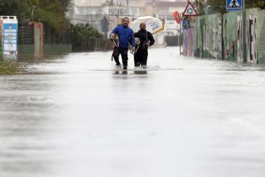 Dos personas abandonan con sus perros la zona de la playa de Bellreguard (Valencia) a través de una calzada inundada este lunes