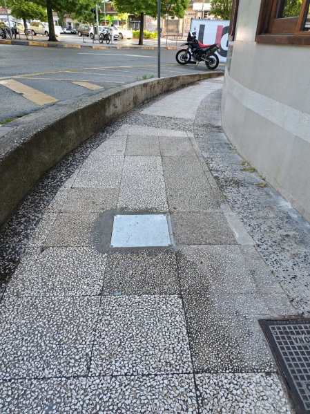 Calle Vuelta del Castillo de Pamplona, a la altura de la Jefatura de Tráfico. Tapa de arqueta metálica estanca totalmente lisa en medio de la acera. No indicada para vía pública, al ser resbaladiza con el pavimento mojado.