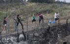 Un grupo de vecinos realiza una cadena con cubos para apagar los rescoldos humenates de una franja de terreno quemada en Muruzábal