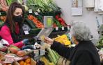 Una persona mayor entrega una tarjeta a la dependienta de una frutería para pagar la compra recién realizada en un puesto del mercado del Ensanche