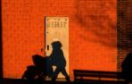 Una mujer empuja una silleta de bebé y su sombra se proyecta en la fachada de la pared de una bajera