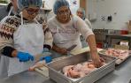 Dos de las personas participantes en el taller preparan los muslos de pollo que se van a cocinar