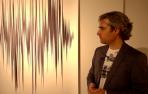 El artista Javier Navarro, junto a una de sus creaciones realizada con bolígrafo negro y regla, que forma parte de la exposición "Vacío leve