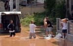 Varios hombres mueven sacos de arena en una calle inundada por la tormenta Daniel