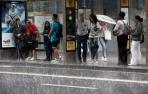 Varias personas se resguardan de la lluvia en una marquesina en Pamplona