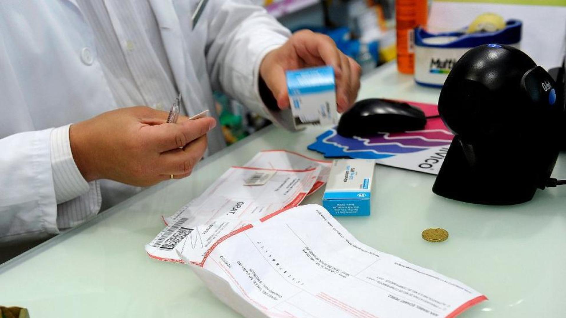 Un farmac&eacute;utico, dispensando medicamentos a un pensionista, este domingo