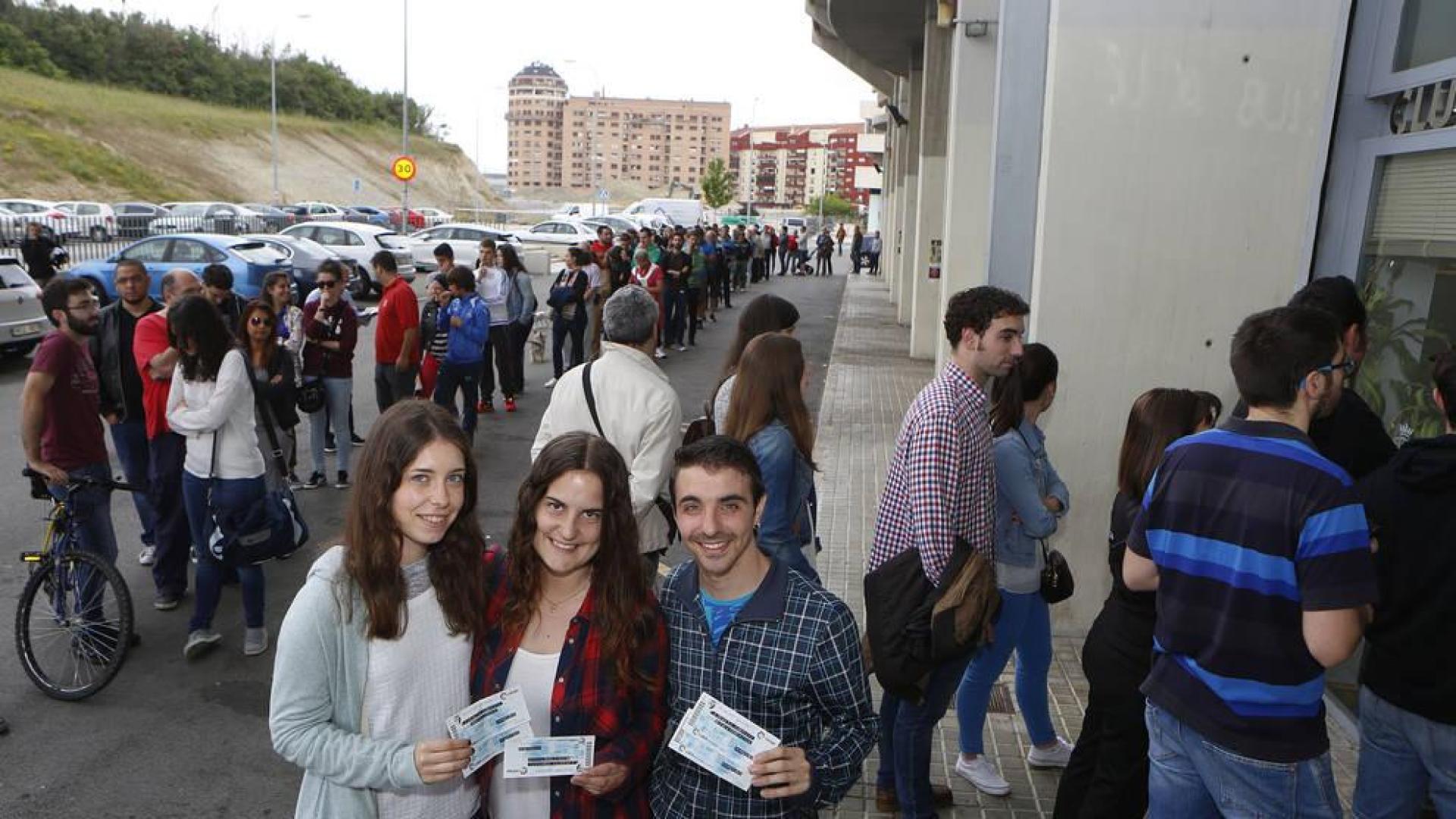 Tres aficionados rojillos posan orgullosos con sus entradas mientras cientos de personas hacen cola a sus espaldas para adquirir una.