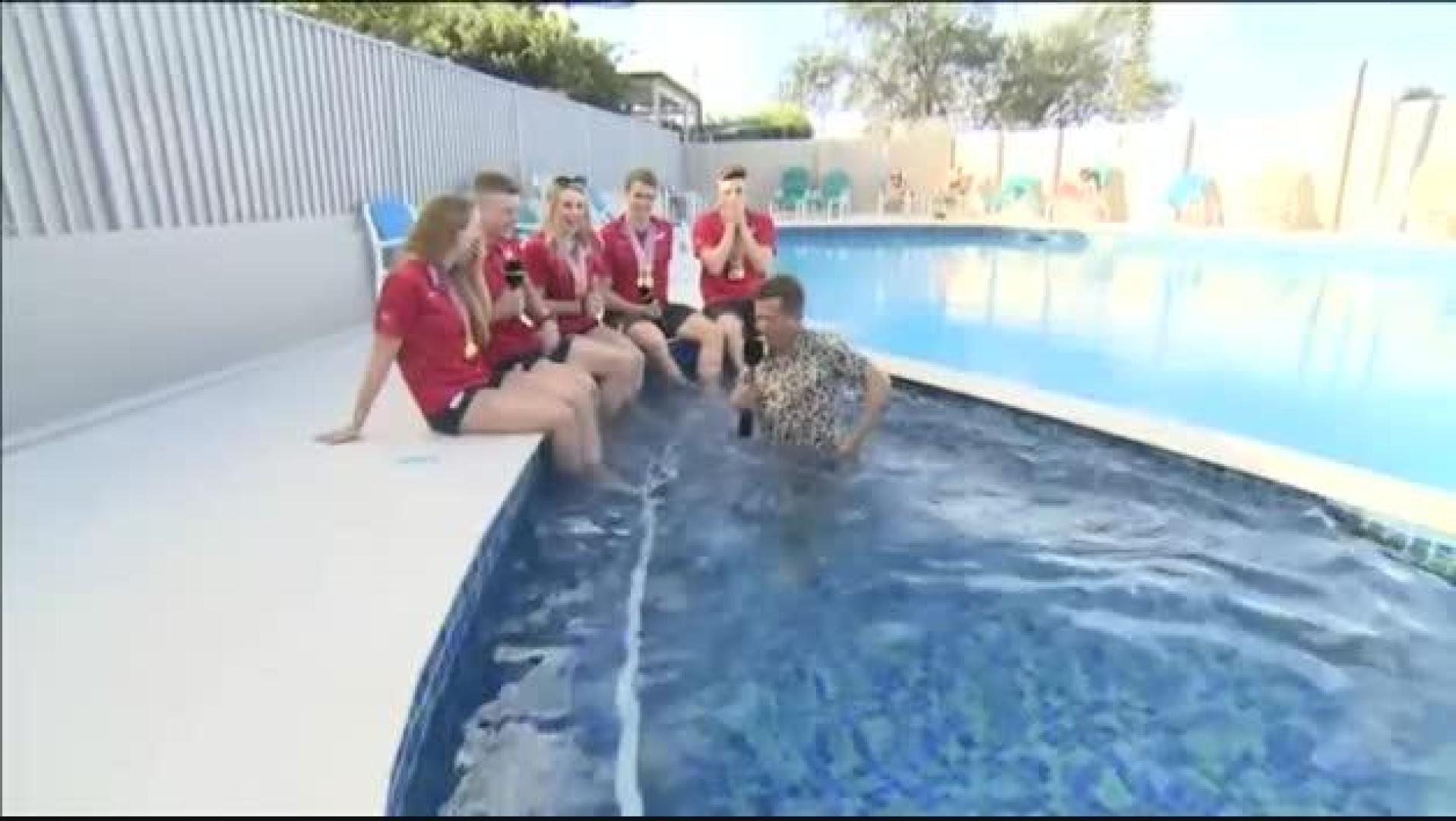Entrevista a unos nadadores, tropieza y se sumerge en la piscina
