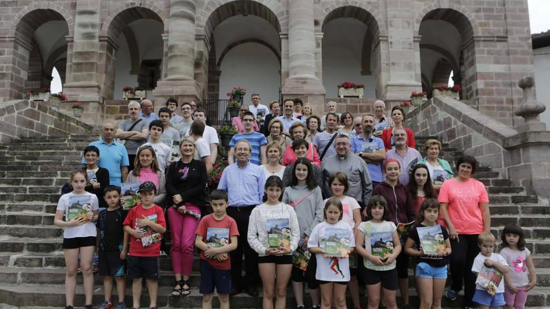 Los visitantes a la presentación de Conocer Navarra y los interventores posan con la revista frente a la iglesia de Ziga.