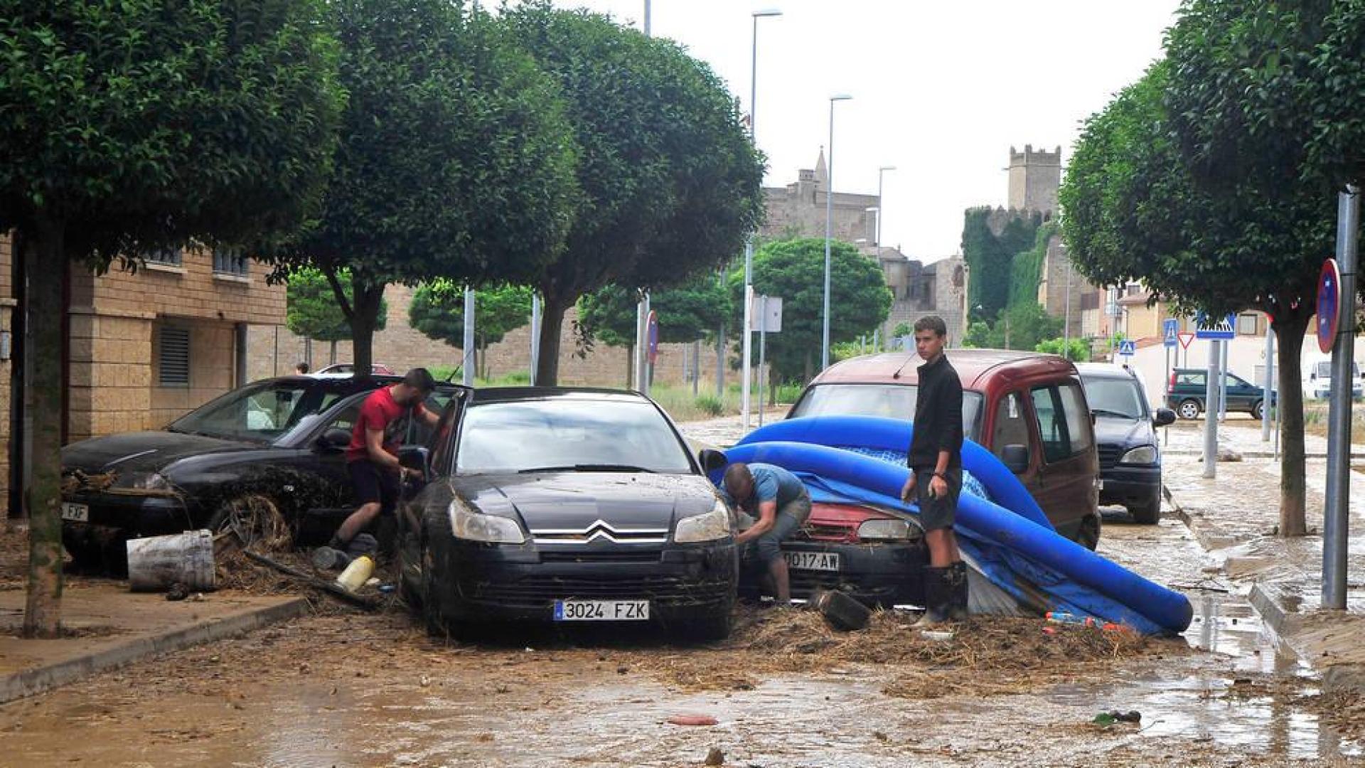 Varios jóvenes intentan desatrapar un coche en una calle de Olite totalmente embarrada con la torre del castillo, al fondo.