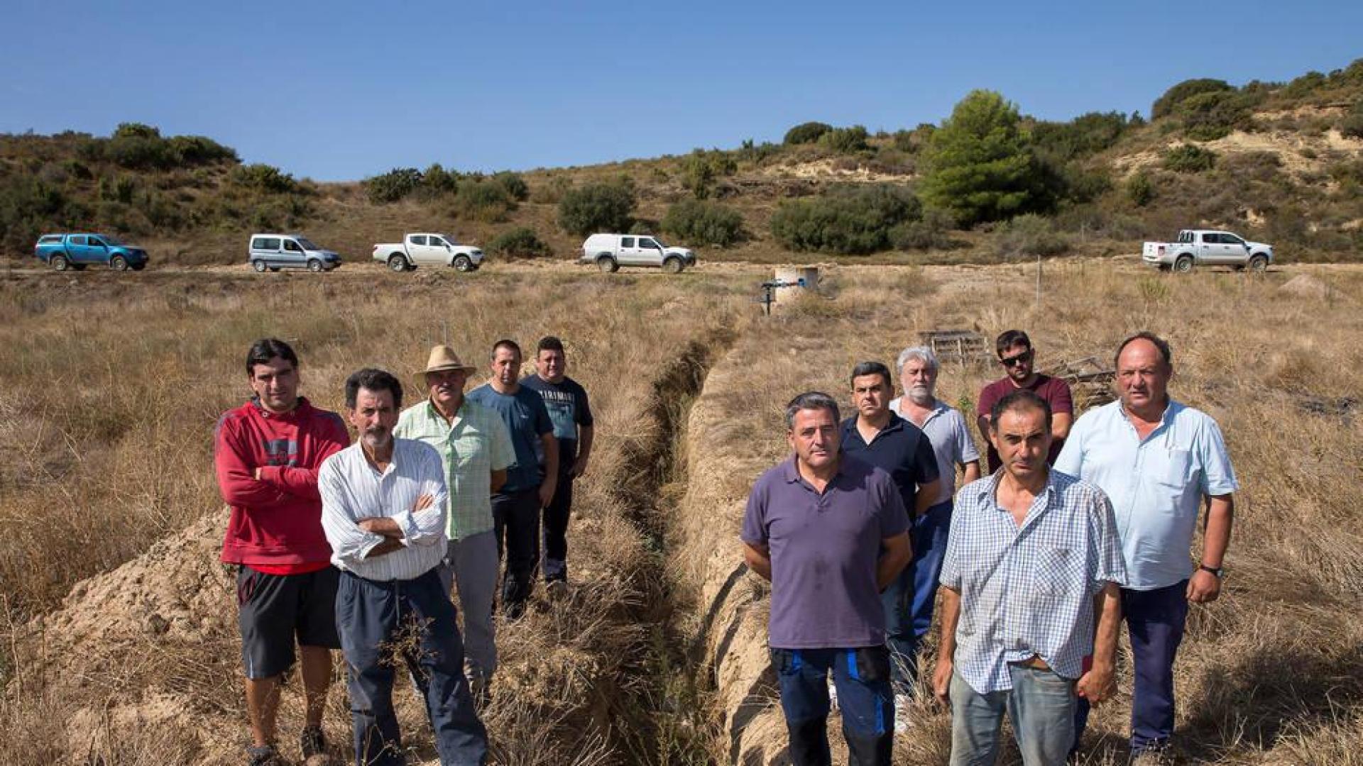 Un grupo de agricultores en una zona de comunal donde se abrieron zanjas y se colocaron tubos para el agua y palos, pero luego se paralizó la obra sin terminarla. De delante hacia atrás, en el lado izquierdo: Ángel Esparza Lacruz, Jon Vallés Gabari, Vitorino Lanas Napal, Ecequiel Murillo Fadrique y Víctor Gurpegui. En el lado derecho: Javier Ramón Gárriz Gárriz, Casimiro Vallés Salaberri, Pascual Lanas Olleta,  Isidoro García Gil, Gerardo Gavari Gárriz y Javier Tanco Tanco.