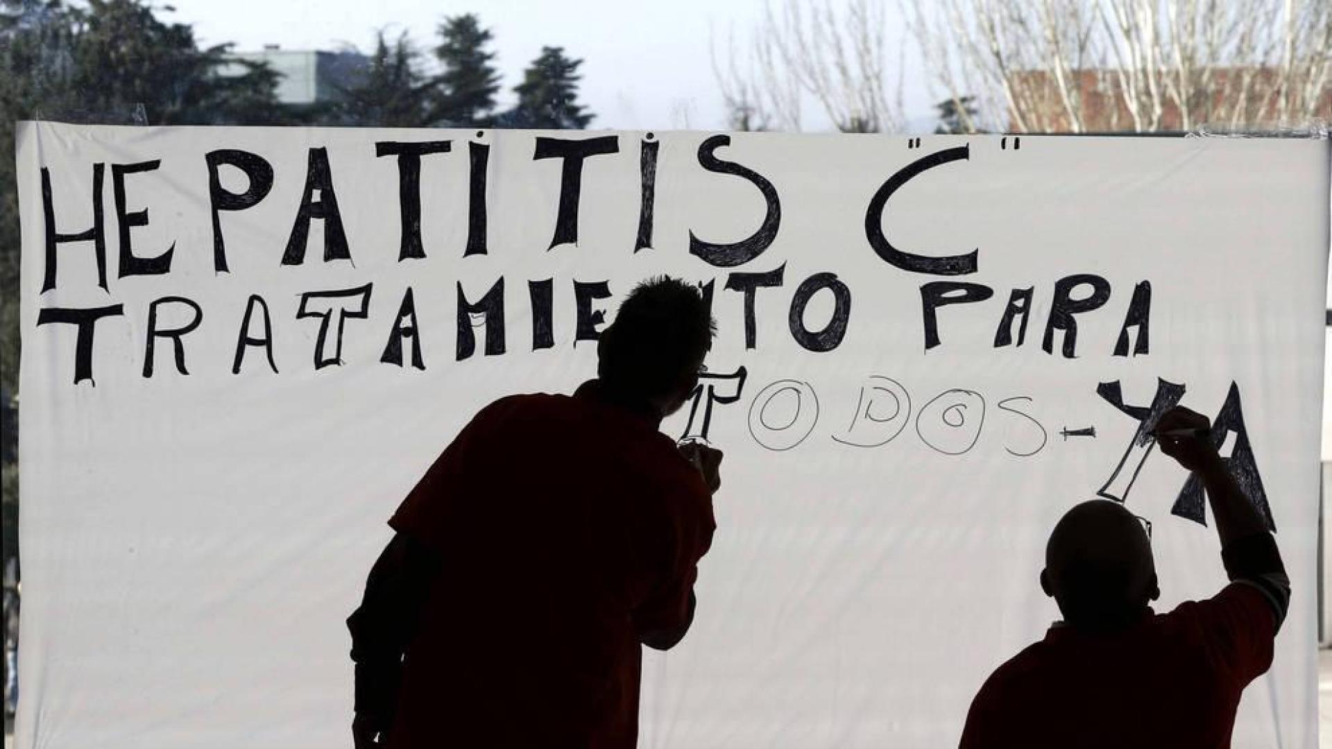 Dos personas teminan de pintar un cartel sobre un cristal en el Complejo Hospitalario de Navarra en favor del tratamiento de la Hepatitis C.