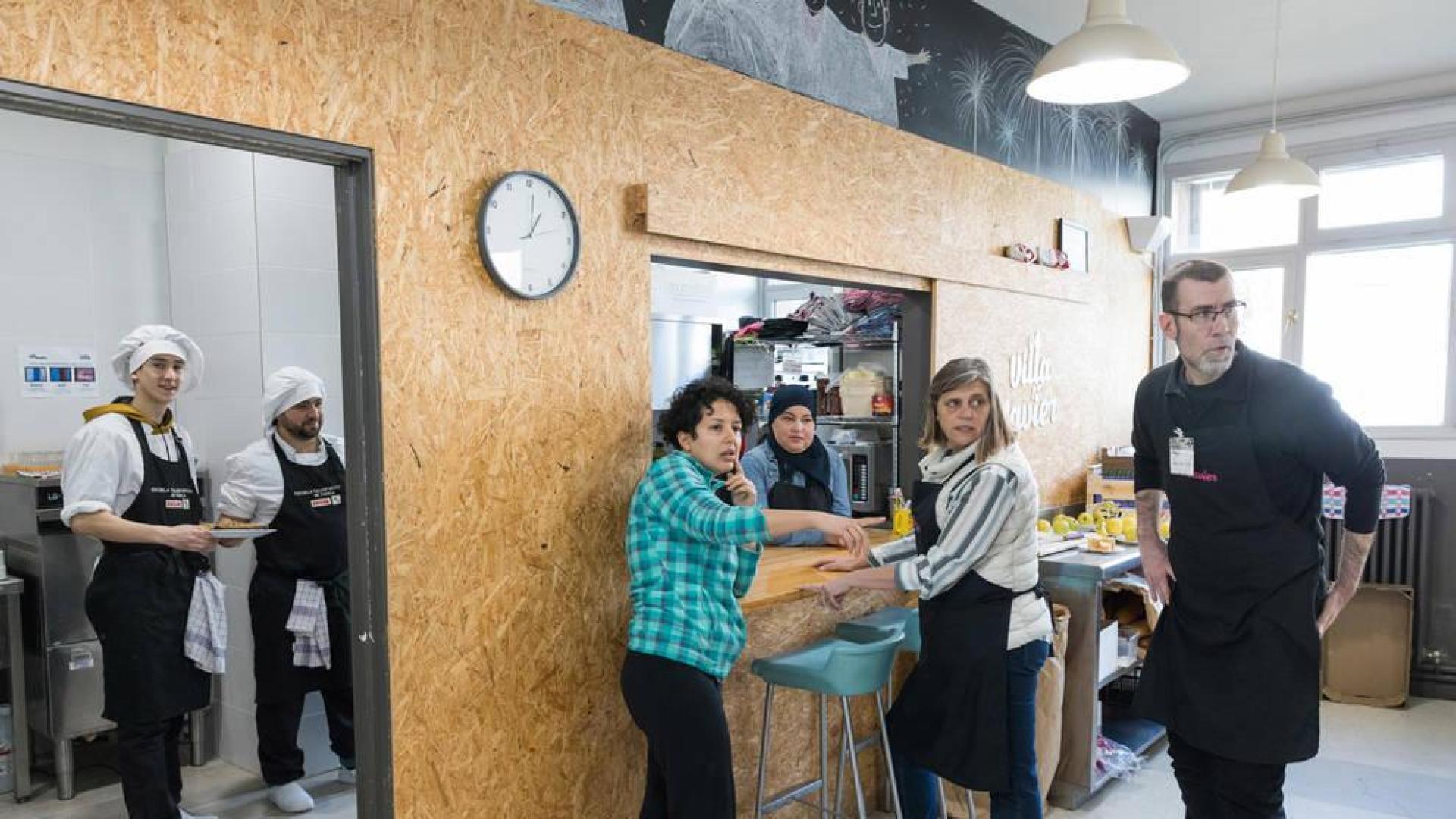 Varios voluntarios del comedor social Villa Javier Tudela se disponen a servir los platos a los usuarios.