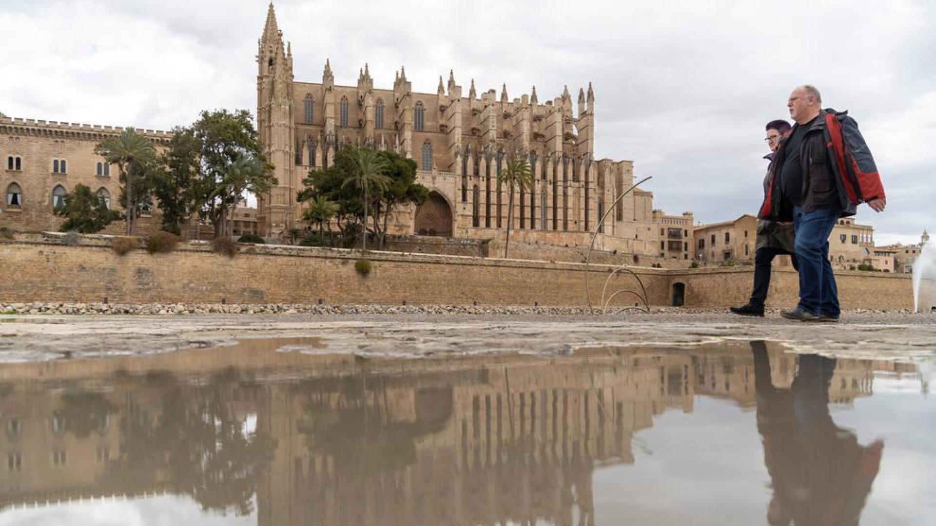Dos viandantes pasan junto a un charco cerca de la catedral de Palma de Mallorca.