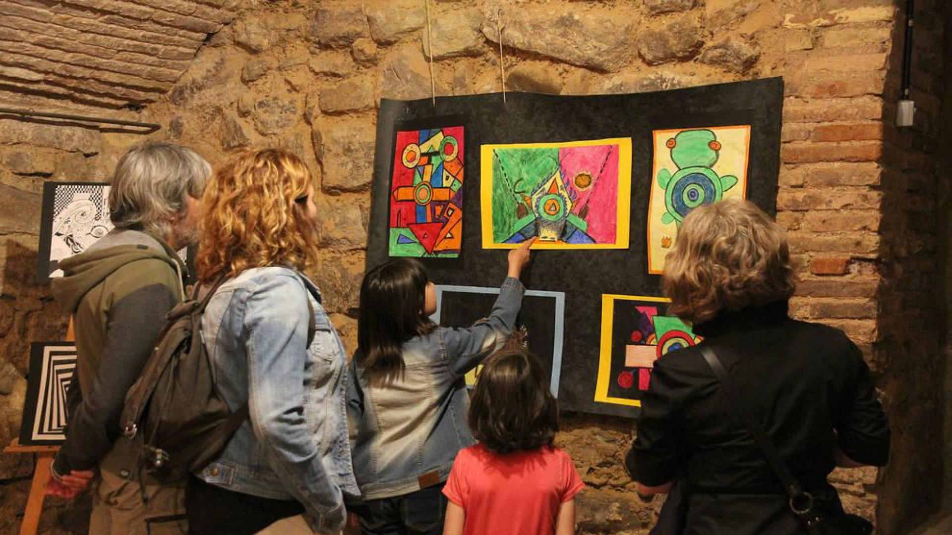 Padres y alumnos contemplan una exposición de pintura abstracta realizada por escolares.