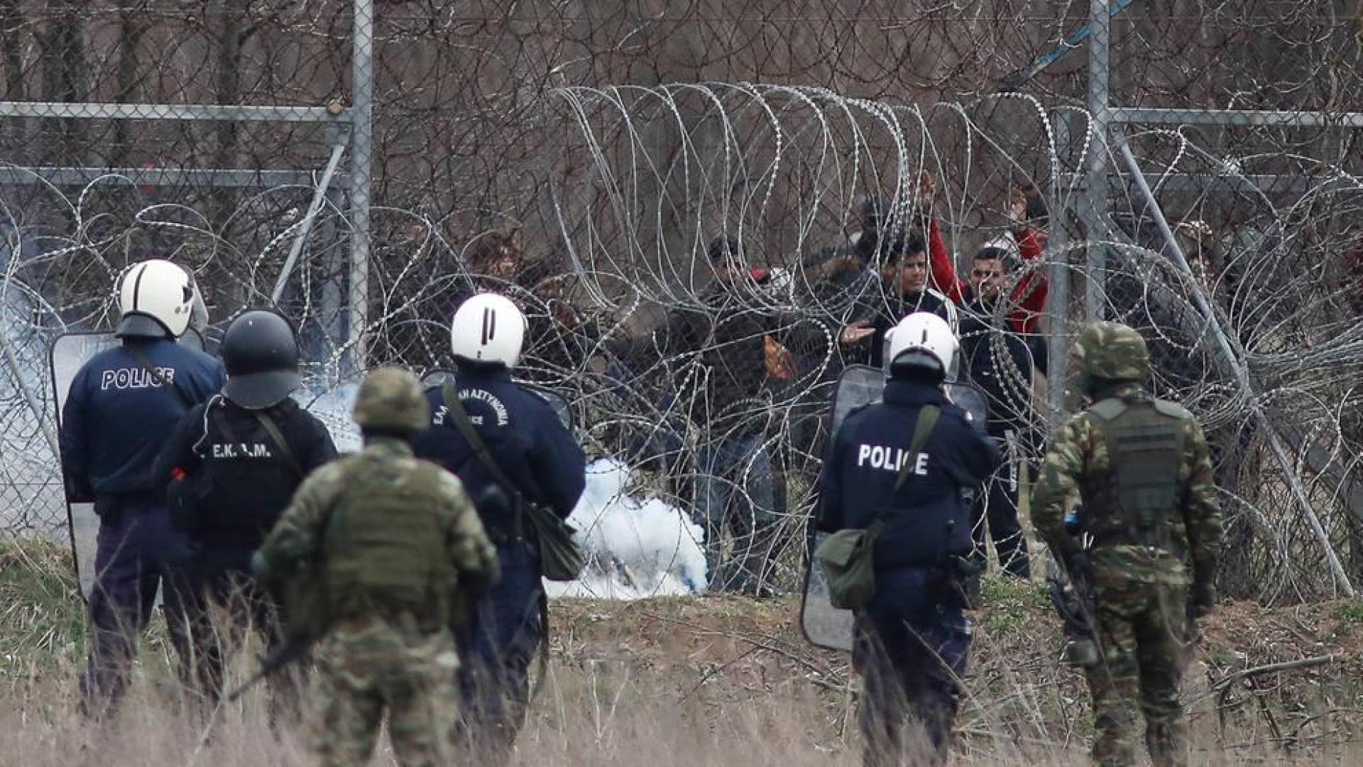 Un grupo de migrantes intenta de cruzar la frontera griega, mientras la policía trata de evitarlo lanzando botes de gases lacrimógenos