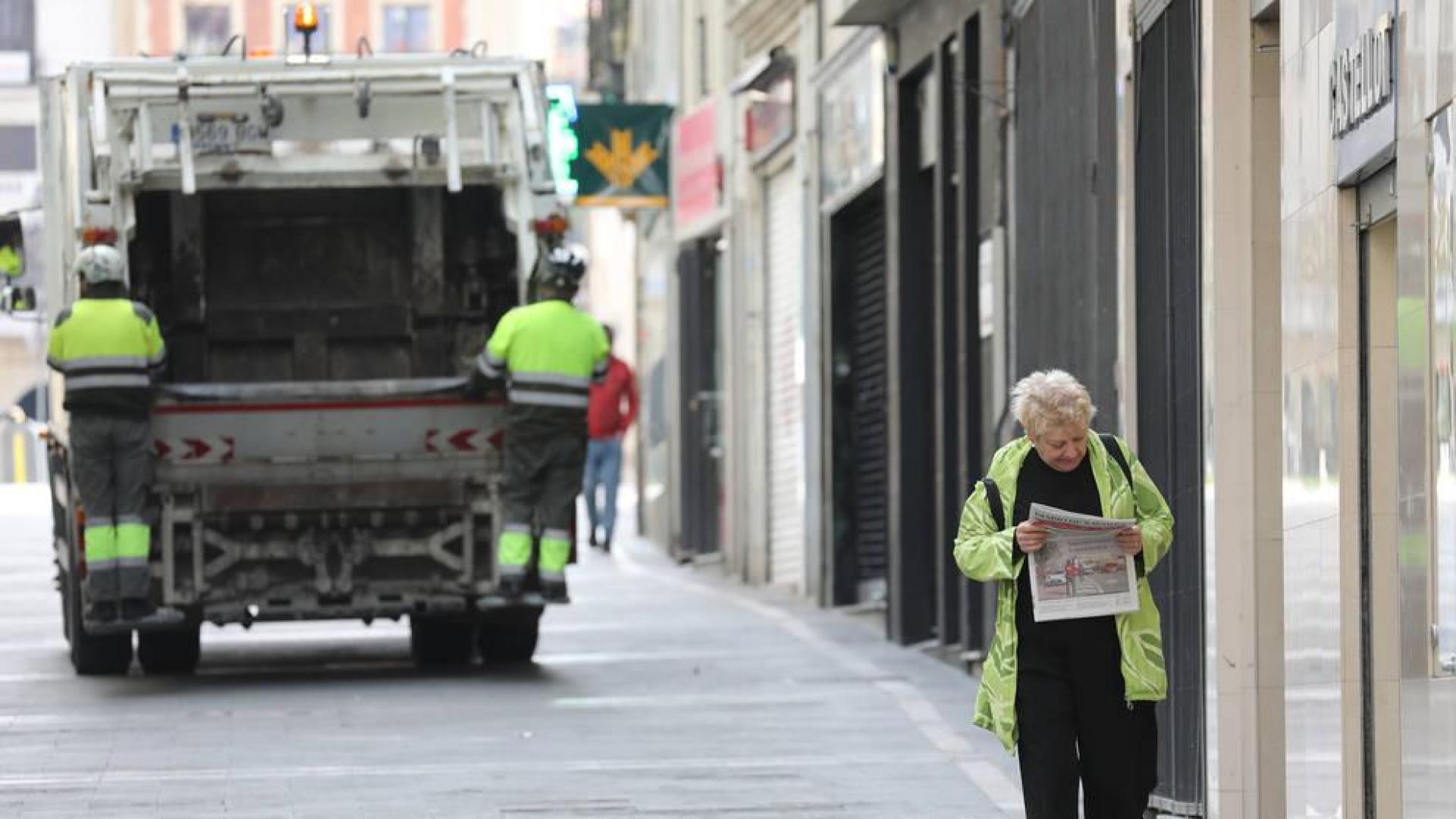 Una mujer regresa de comprar el pan y la prensa en Pamplona. Al fondo, el servicio de recogida de basuras, que sigue funcionando.