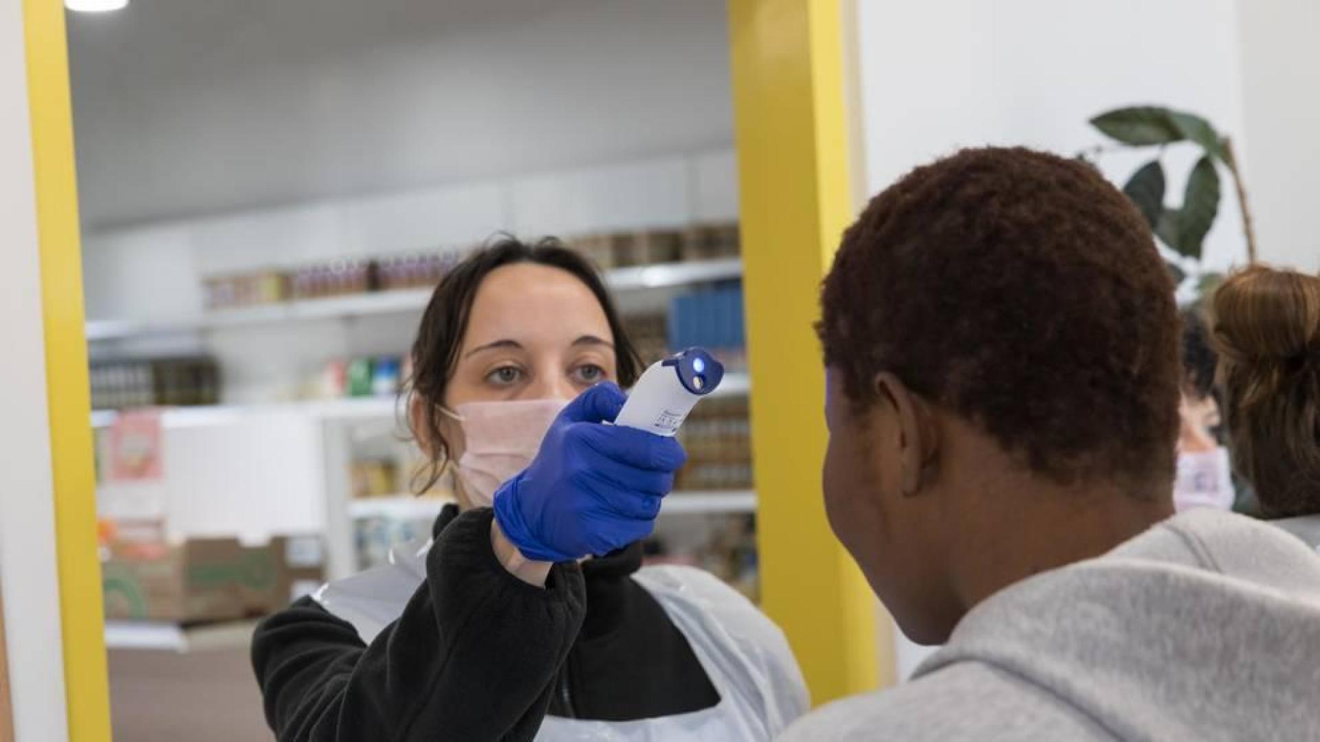 Una voluntaria toma la temperatura a un usuario antes de entrar a 'El Capacico'.
