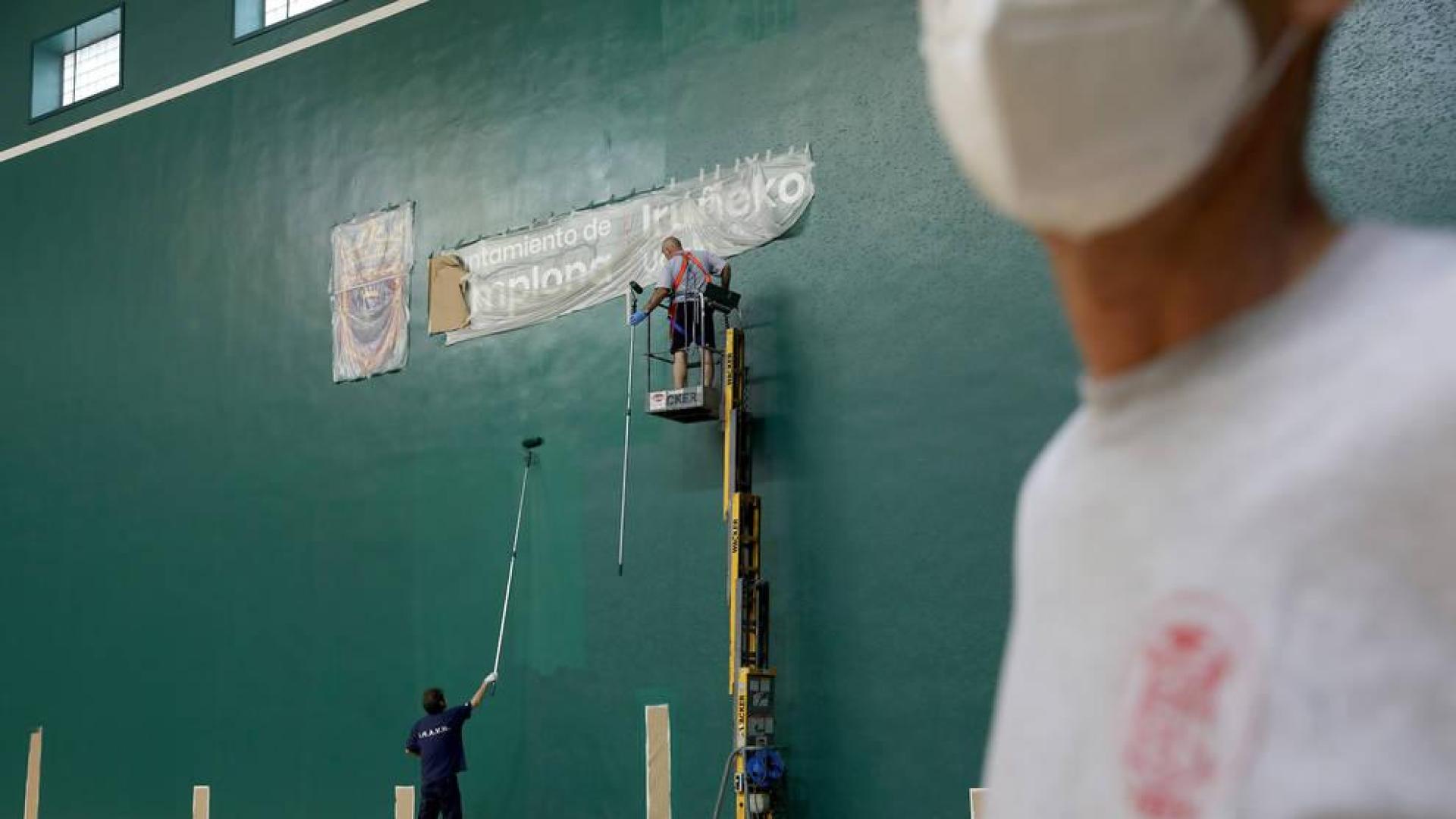 Dos operarios de la Federación Navarra de Pelota pintan la pared izquierda del Labrit este lunes por la mañana.