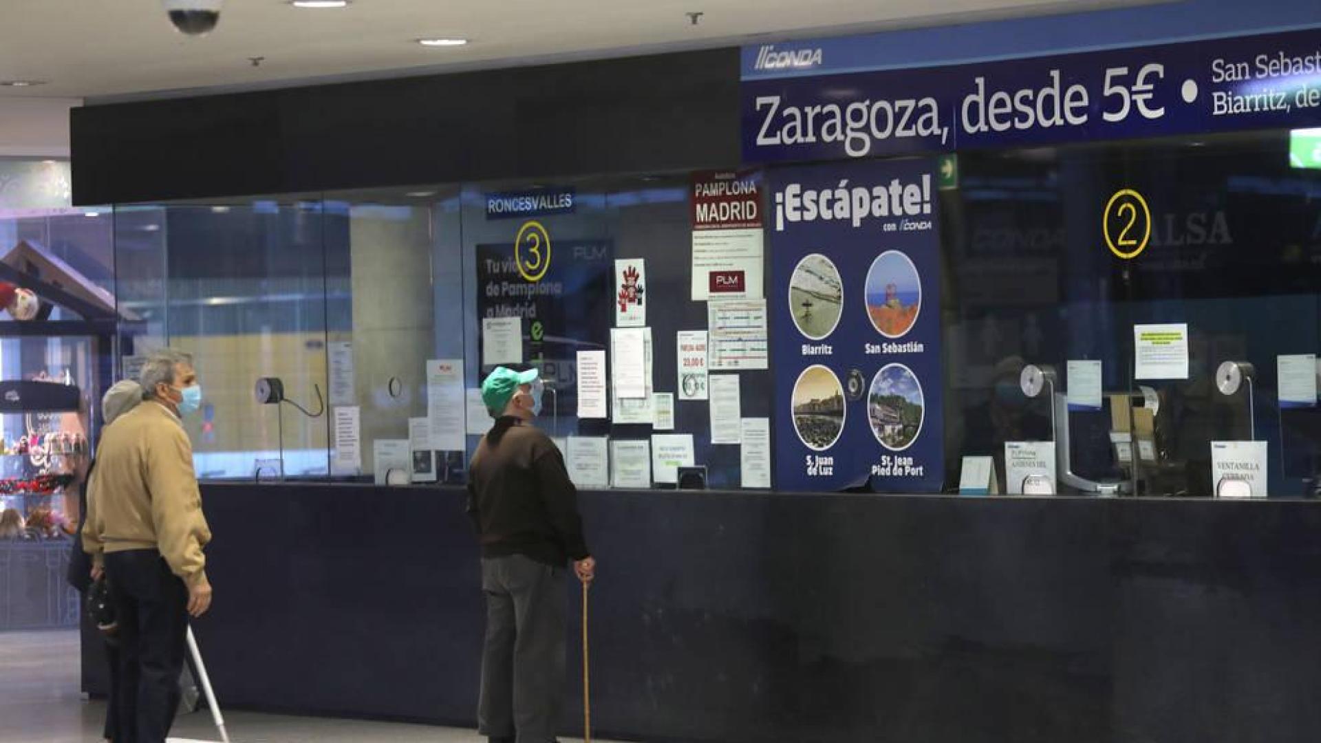 Varias personas aguardan en la taquilla de la estación de autobuses.