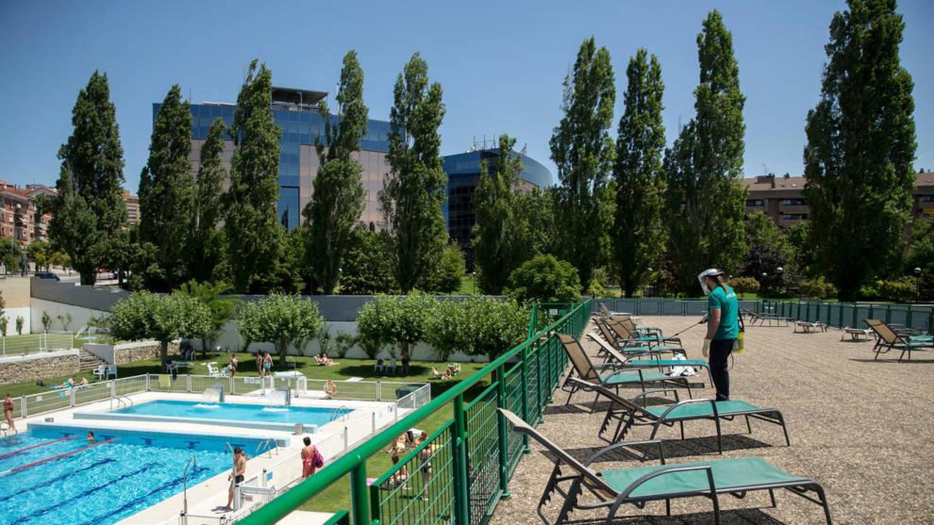 Un empleado desinfecta la zona de las hamacas, al tiempo que varios usuarios disfrutan de las instalaciones de las pisicinas de Oberena.