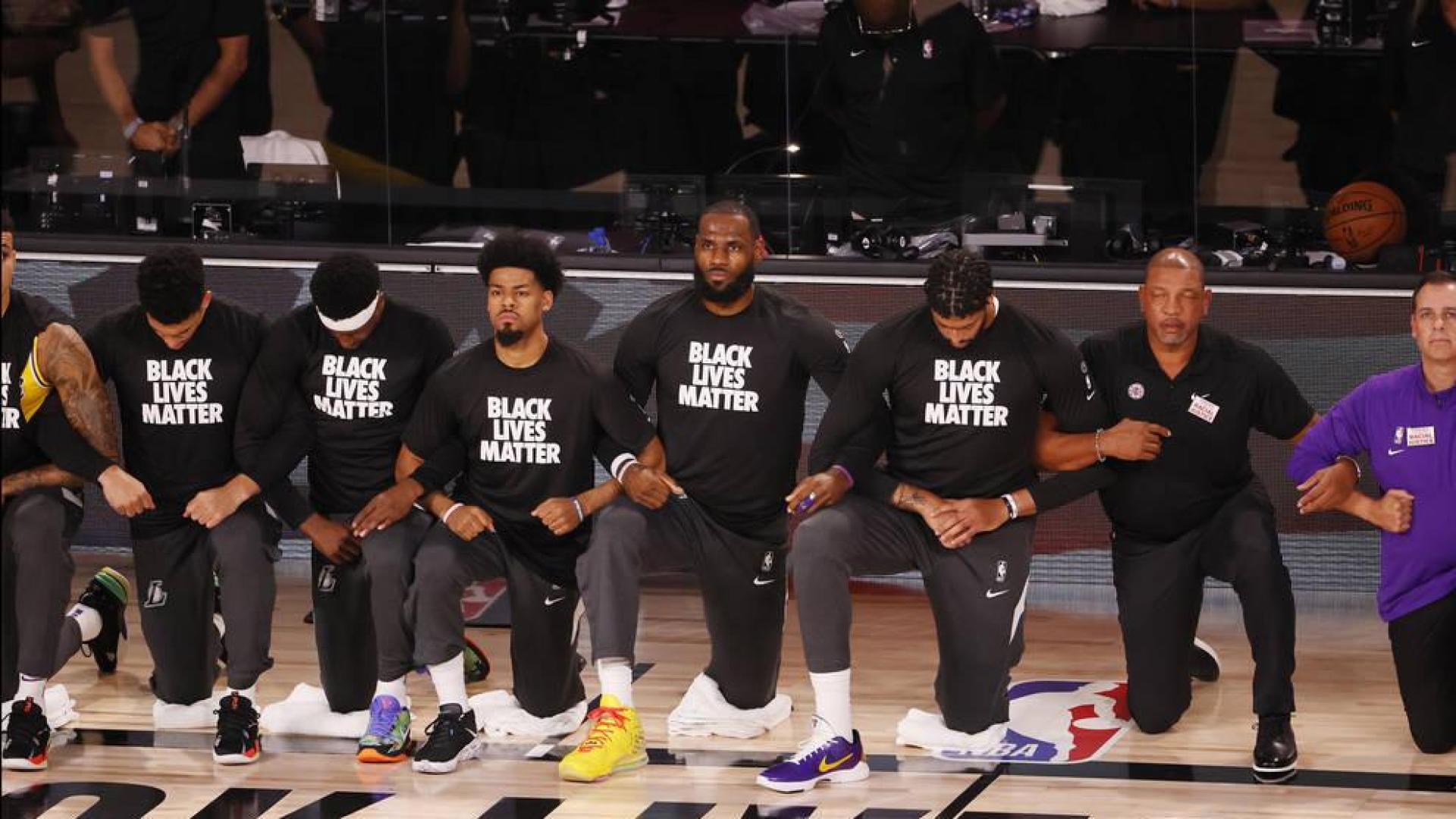 Los jugadores de Los Angeles Lakers y Los Angeles Clippers escuchan el himno con la rodilla en el suelo contra el racismo