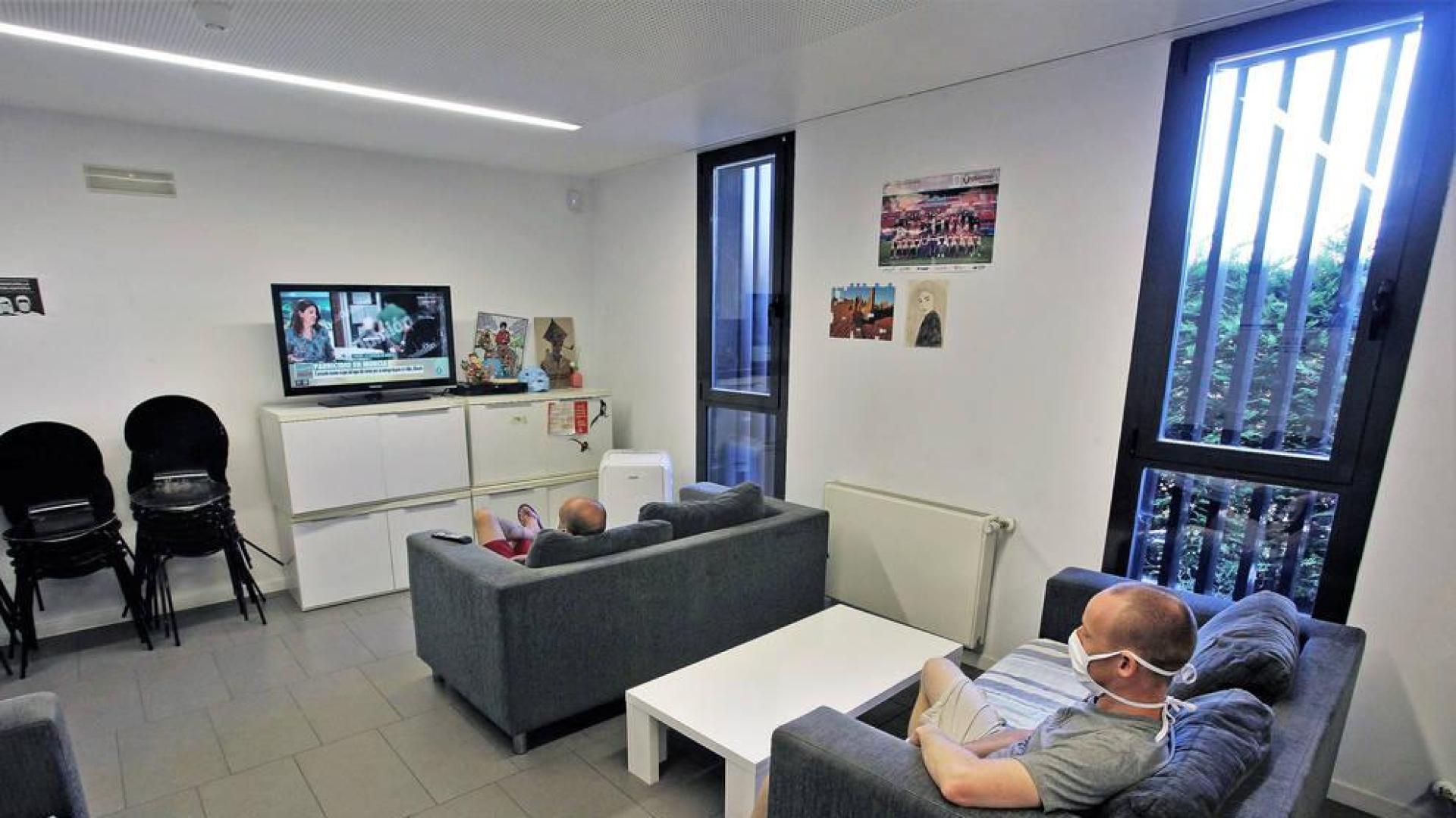 Usuarios del centro para personas sin hogar de Triniarios ven la televisión guardando la distancia.