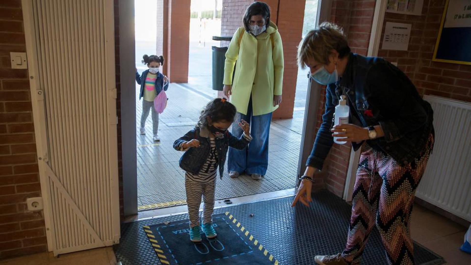 Daniela, de 4 años, desinfecta sus zapatos tras soltar a su madre, con abrigo amarillo, Marta Sampedro.