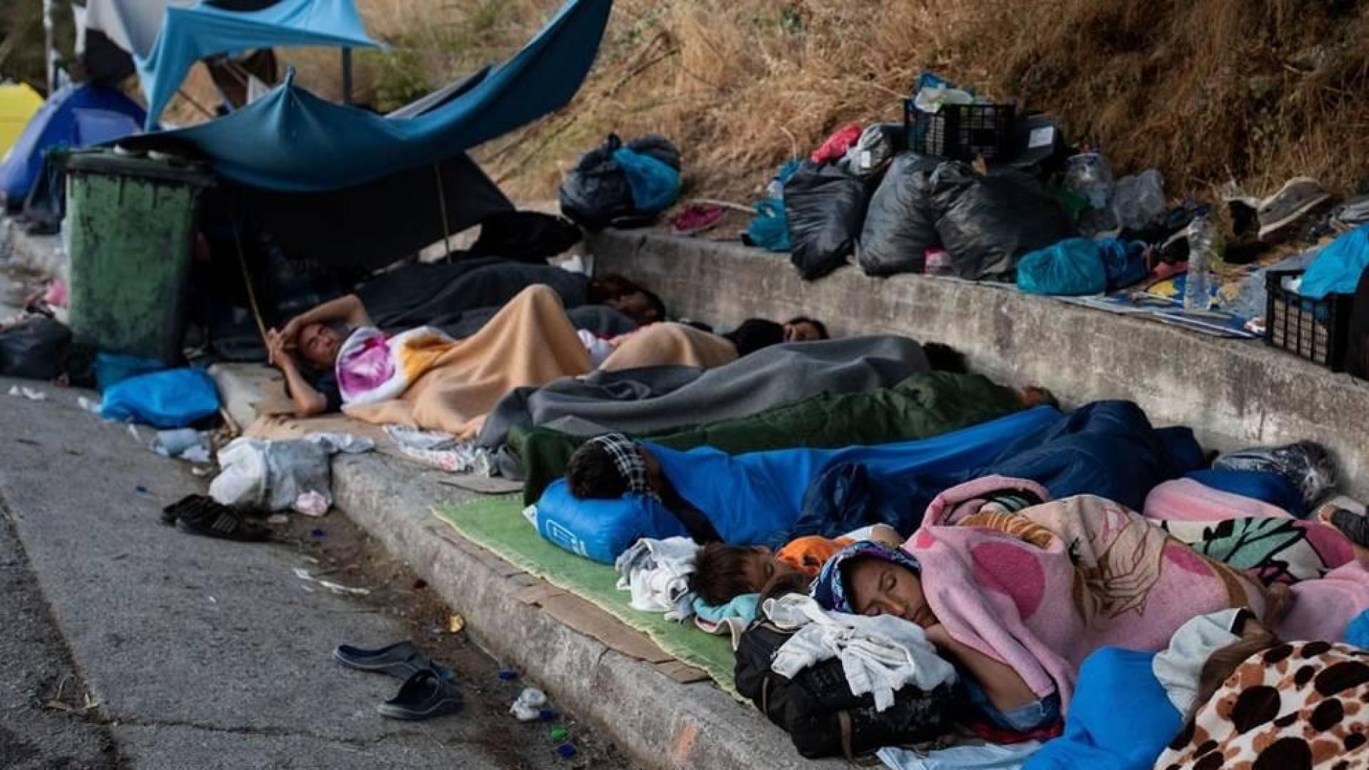Migrantes del campo de Moria duermen junto a una carretera.