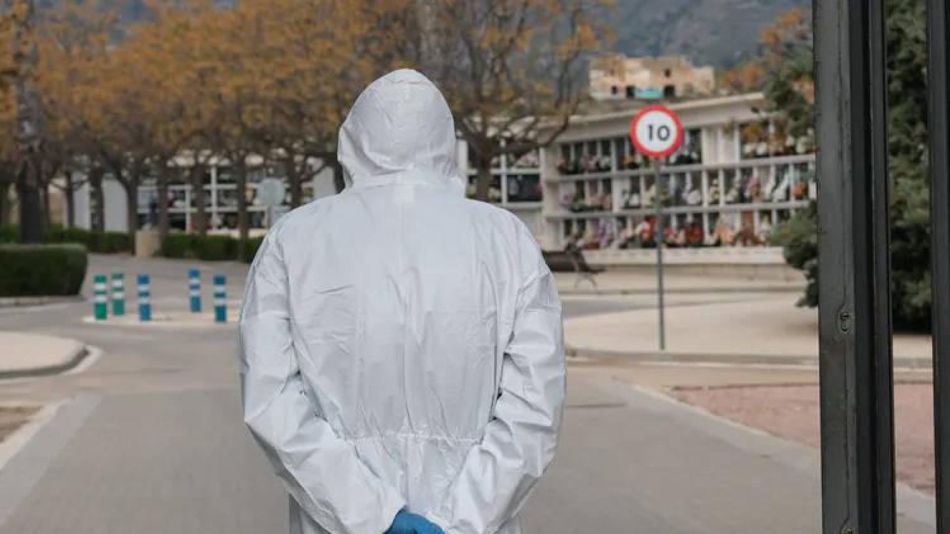 Una persona con un traje de protección, frente un cementerio.