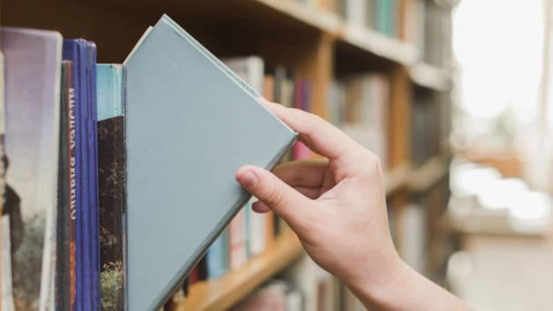 Imagen de una persona tomando un libro de una estantería