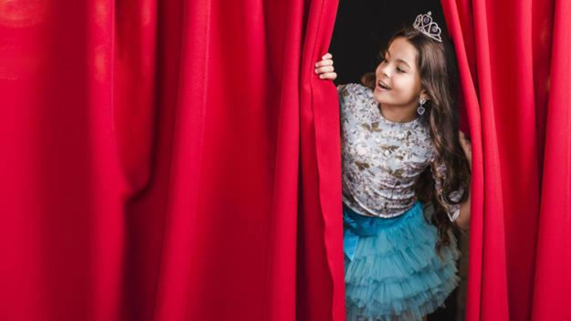 Imagen de una niña tras el telón en un escenario de teatro