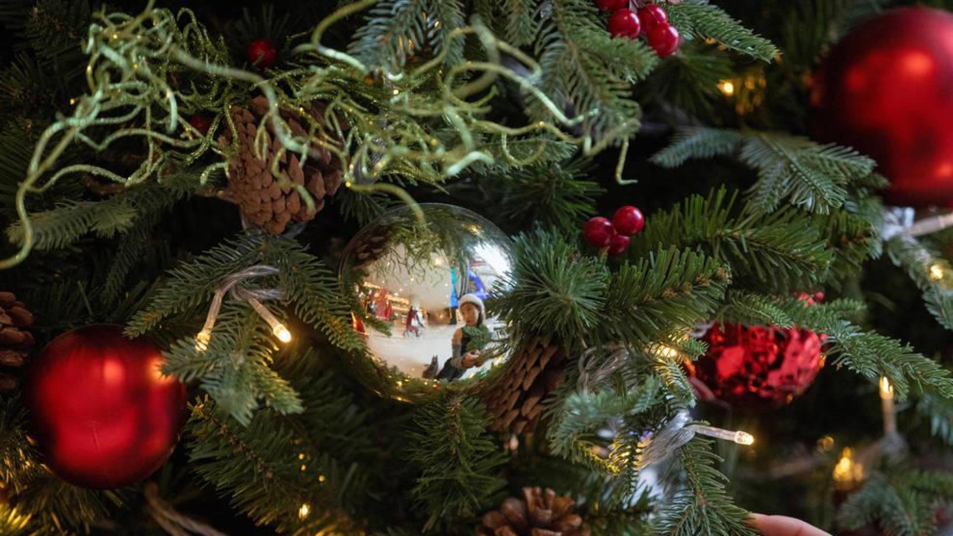 Una mujer, reflejada en la bola de un árbol navideño.