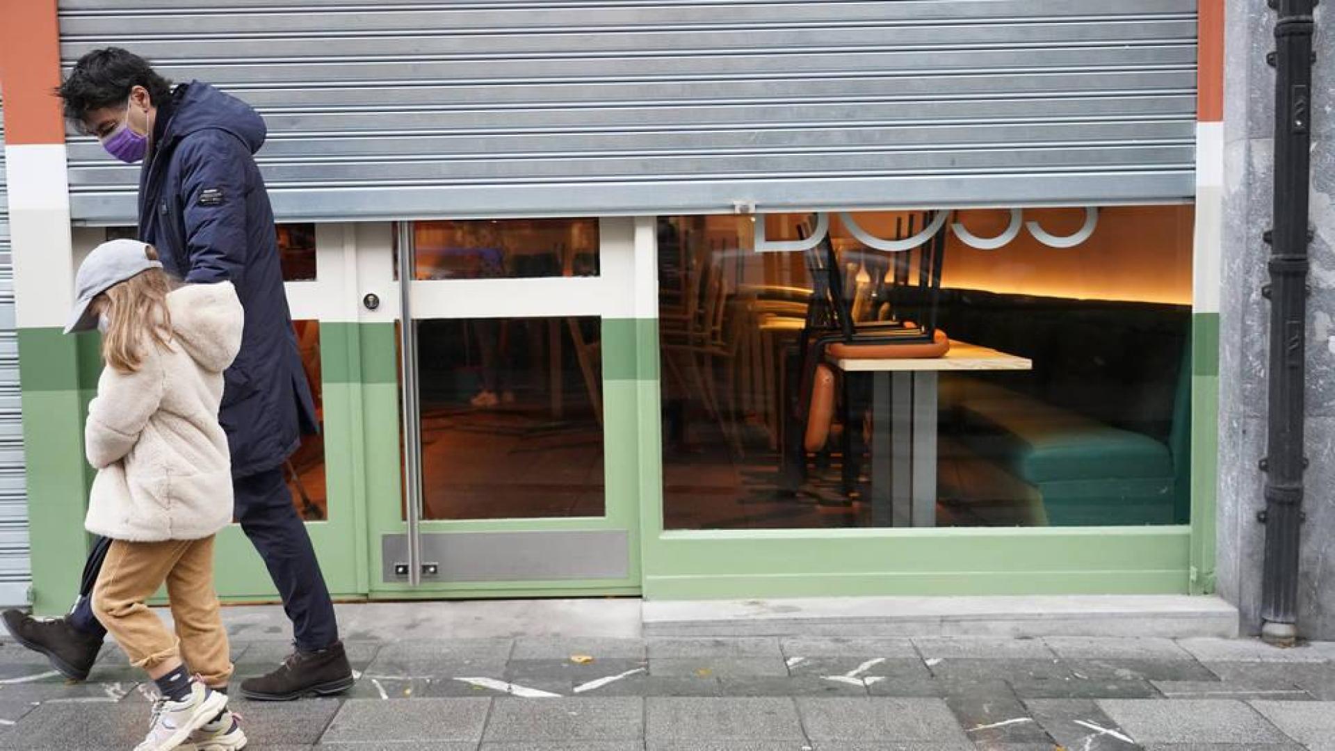 Un hombre y una niña pasan por delante de un establecimiento cerrado en Bilbao.