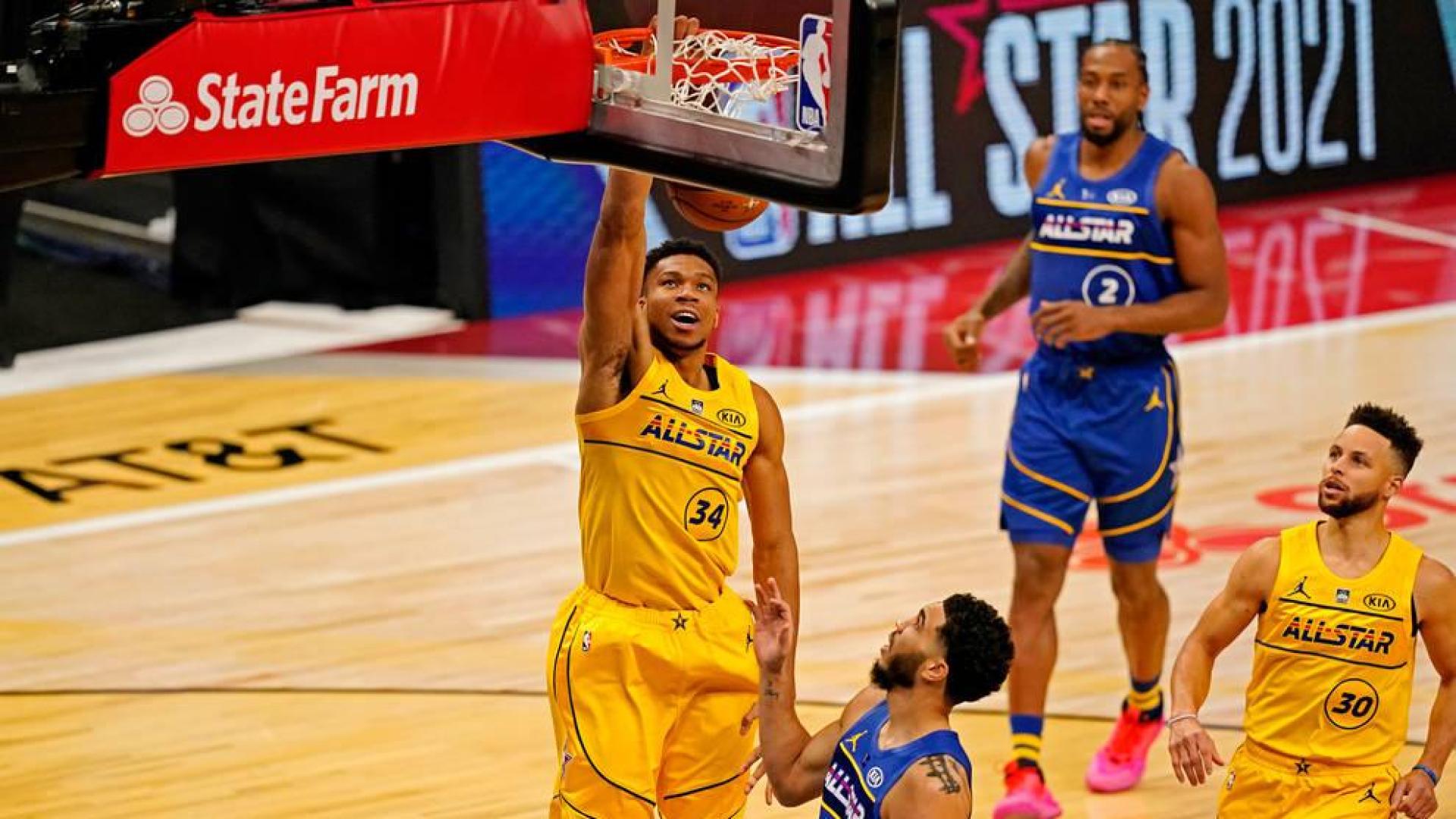Giannis Antetokounmpo anota ante Jayson Tatum. A la derecha, Curry.