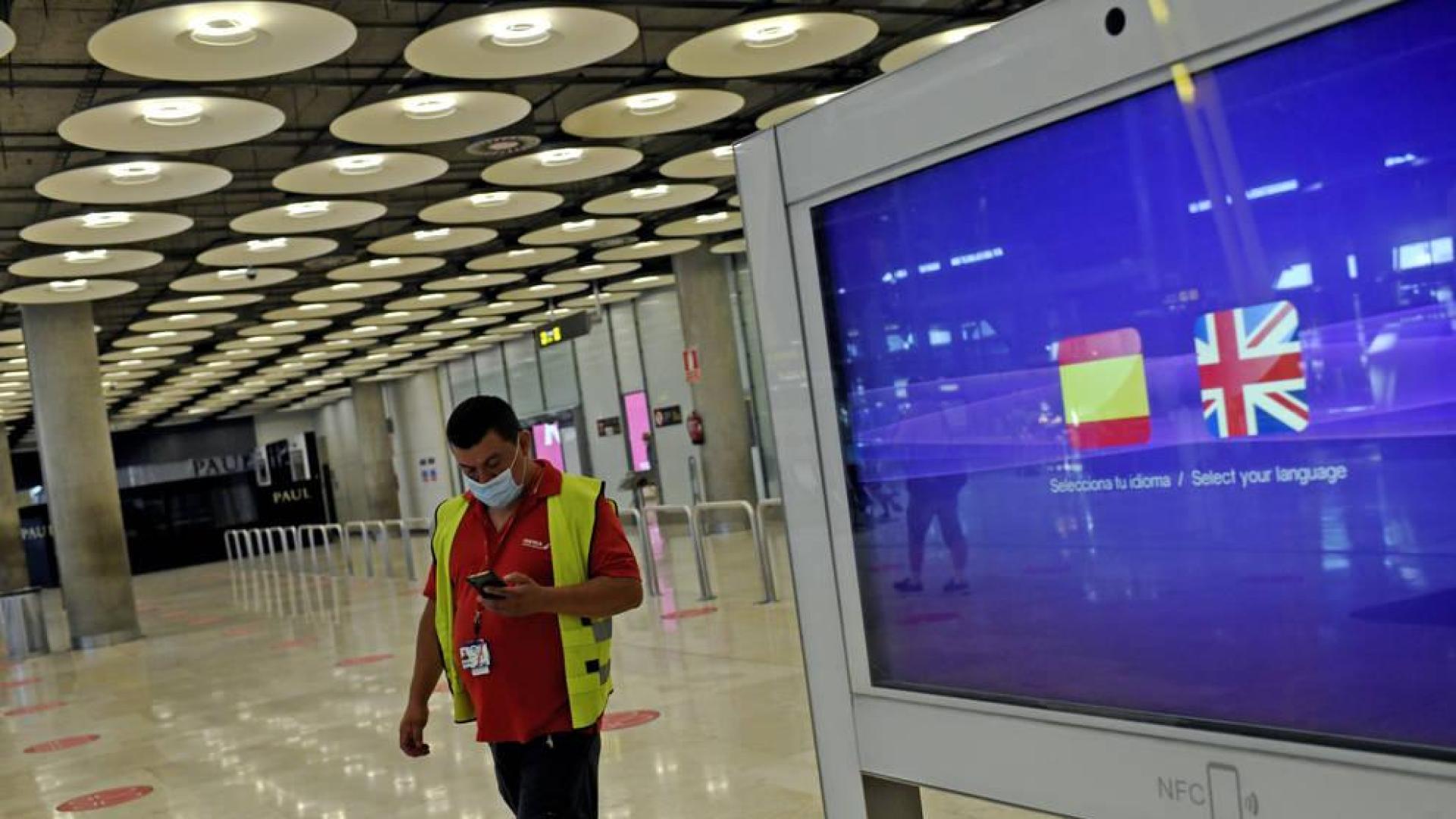 Un operario de Iberia pasa al lado de un monitor con las banderas de España y Reino Unido en la T1 del Aeropuerto de Madrid-Barajas.