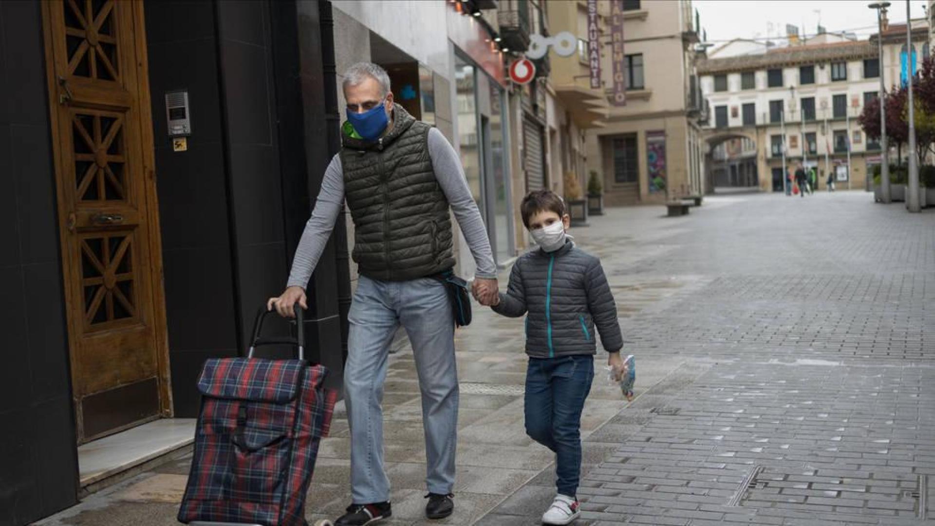 Un niño camina por la calle con su padre, ambos con mascarillas, en Tudela
