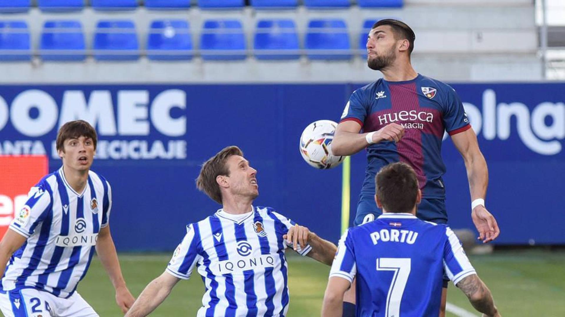 El delantero del Huesca Rafael Mir intenta rematar de cabeza junto a Nacho Monreal de la Real Sociedad