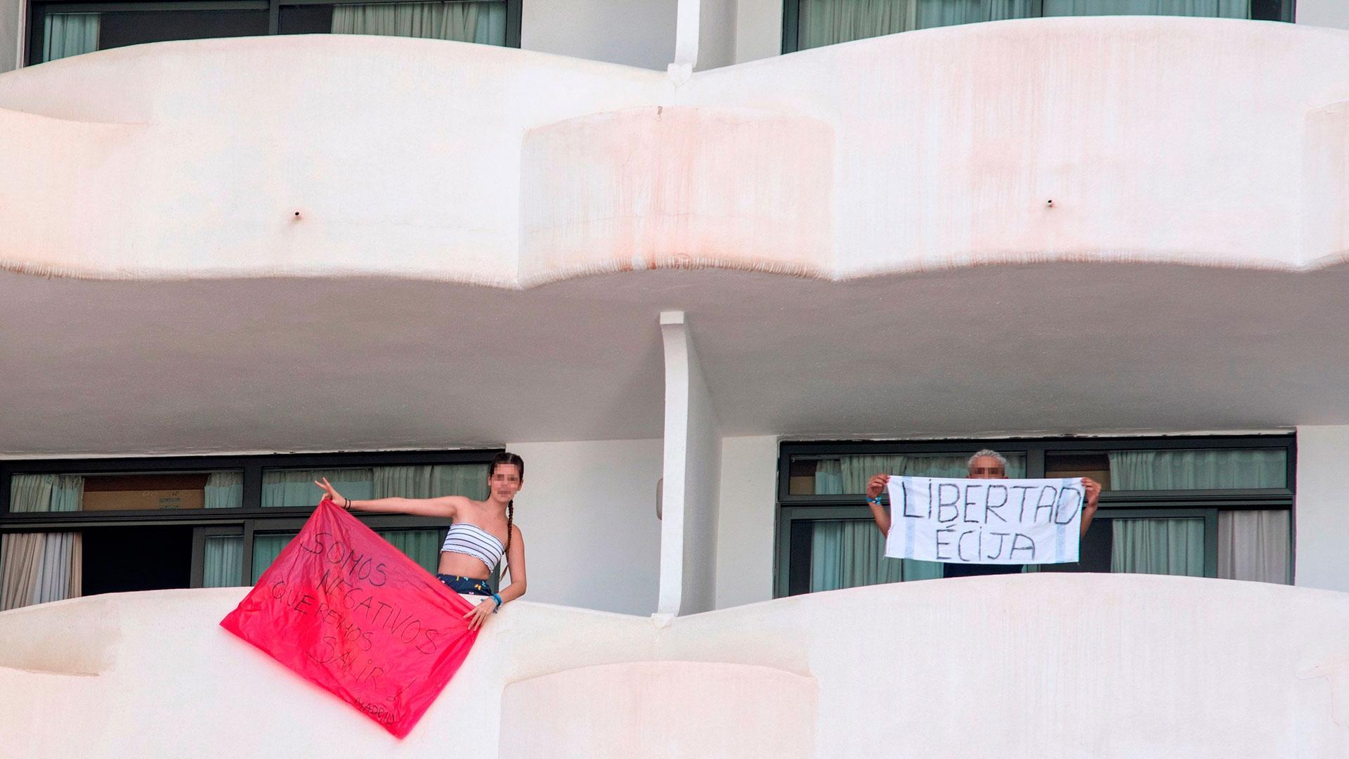 Dos de los jóvenes en aislamiento en el hotel Palma Bellver portan dos pancartas pidiendo salir