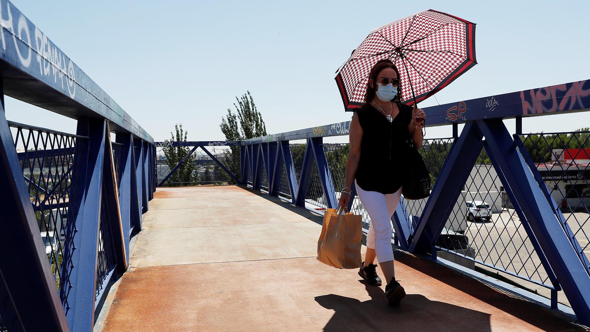 Una mujer con mascarilla se protege del sol cuando cruza por una pasarela en Madrid