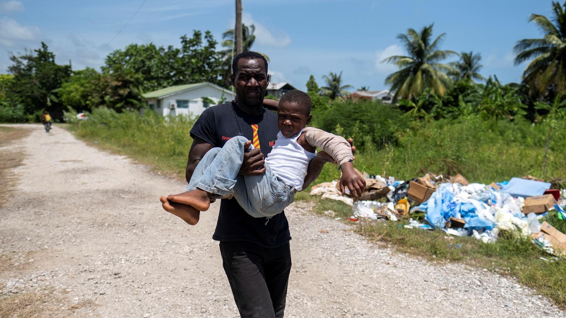 Hombre carga a un niño herido hacia un centro medico para que reciba tratamiento en Les Cayes