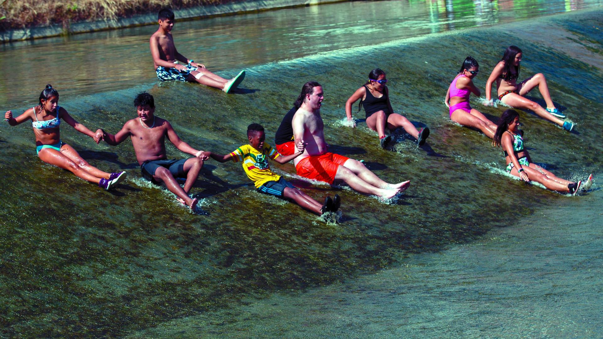 Varios de los participantes en la ludoteca de la Txantrea se deslizan por la presa del río Arga junto a uno de los monitores