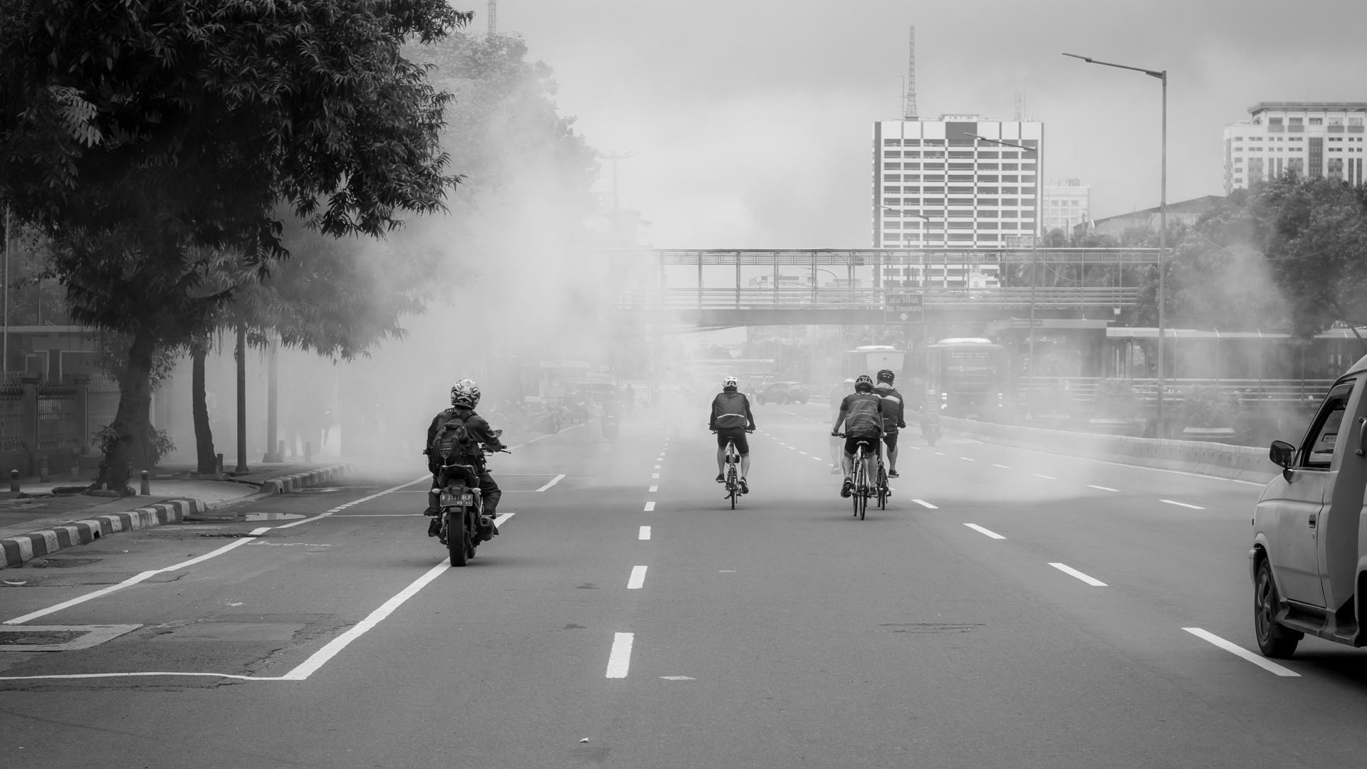 Varias personas circulan en moto o bicicleta entre el humo en una ciudad
