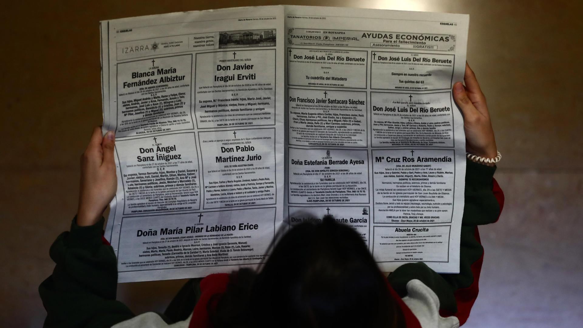 Una mujer lee las páginas de las esquelas en el periódico