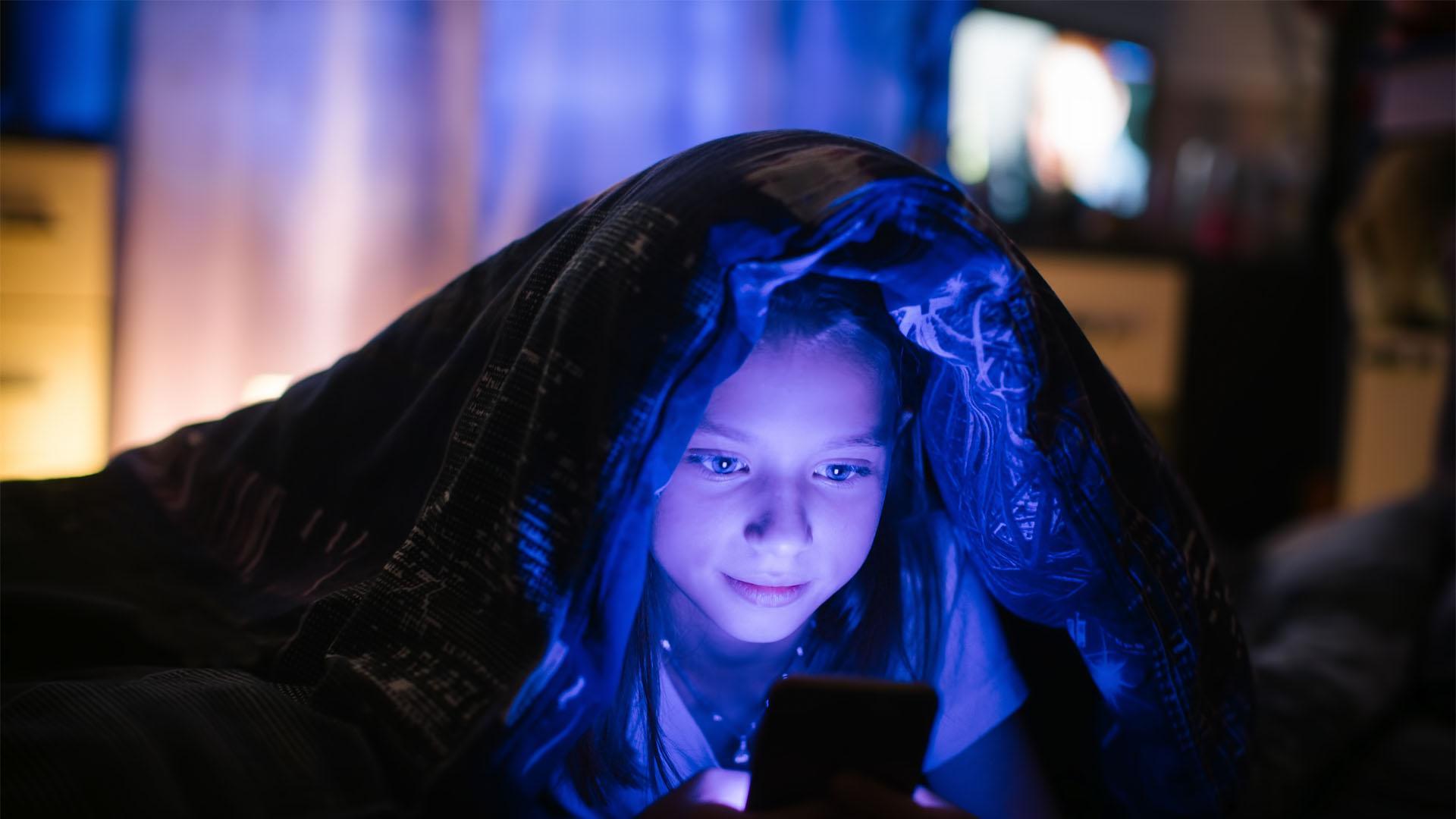 Una niña mira una pantalla por la noche