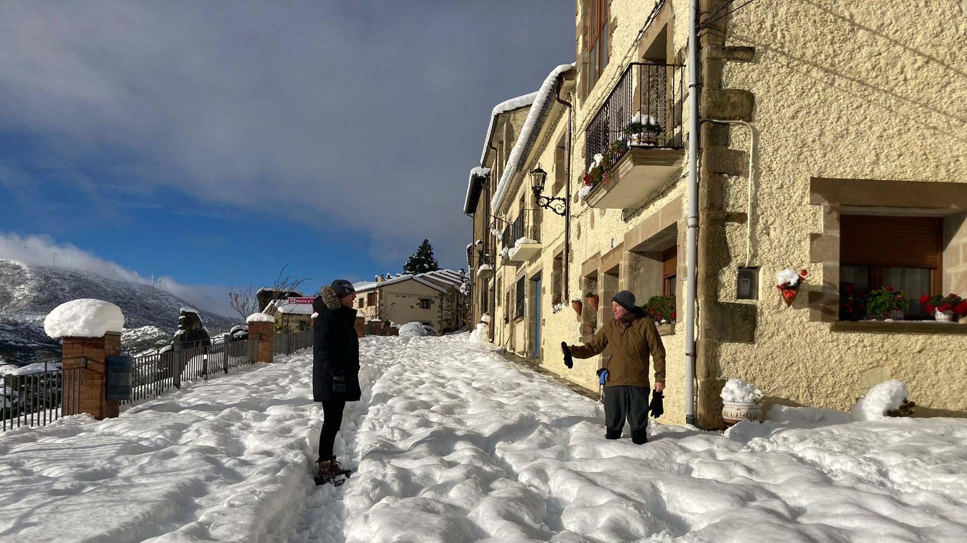 Dos vecinos conversan, ayer, en la carretera de acceso a Petilla de Aragón cubierta por varios cm de nieve