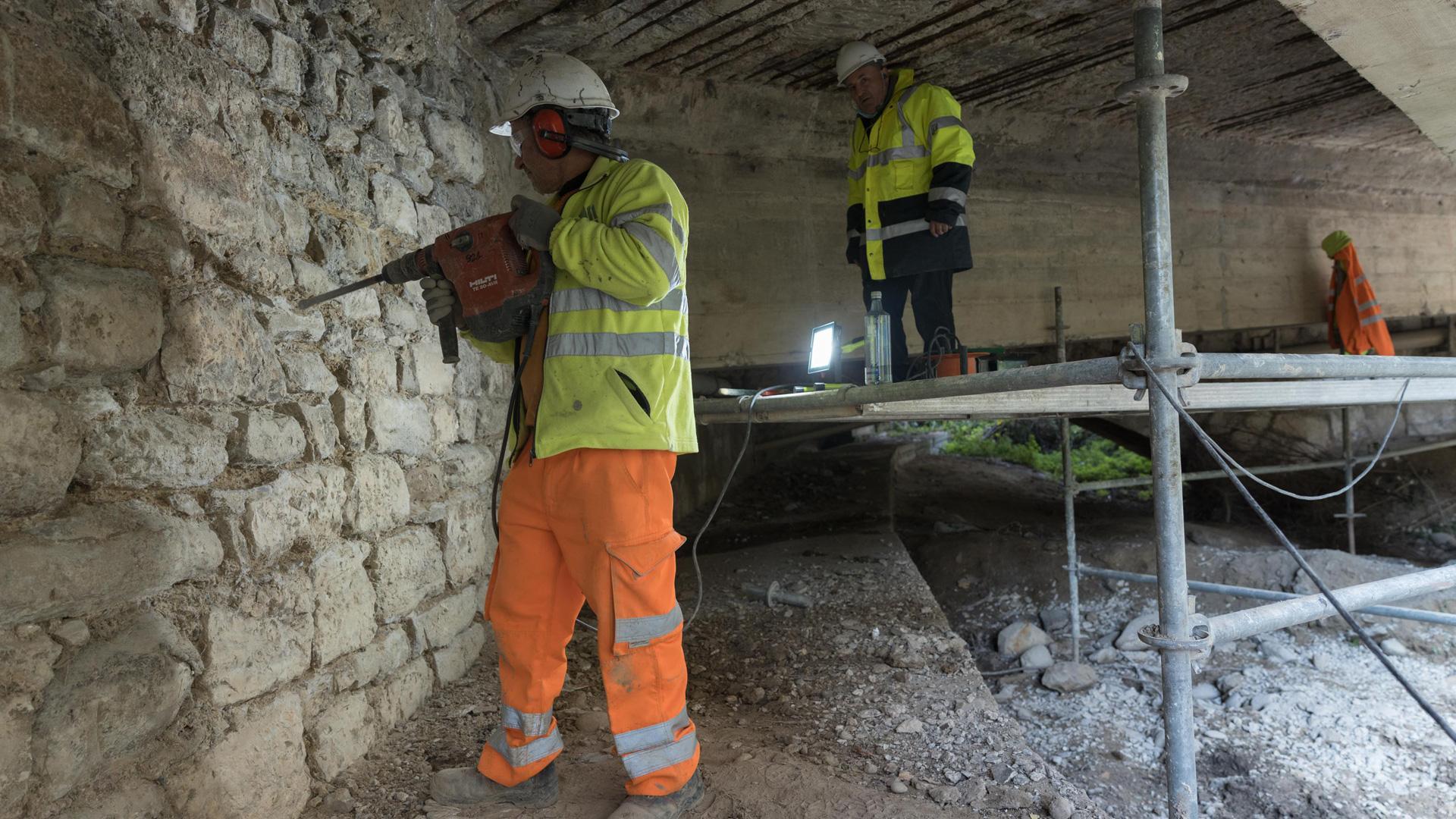 Dos operarios trabajan en los arcos del puente más cercanos al casco urbano de Tudela
